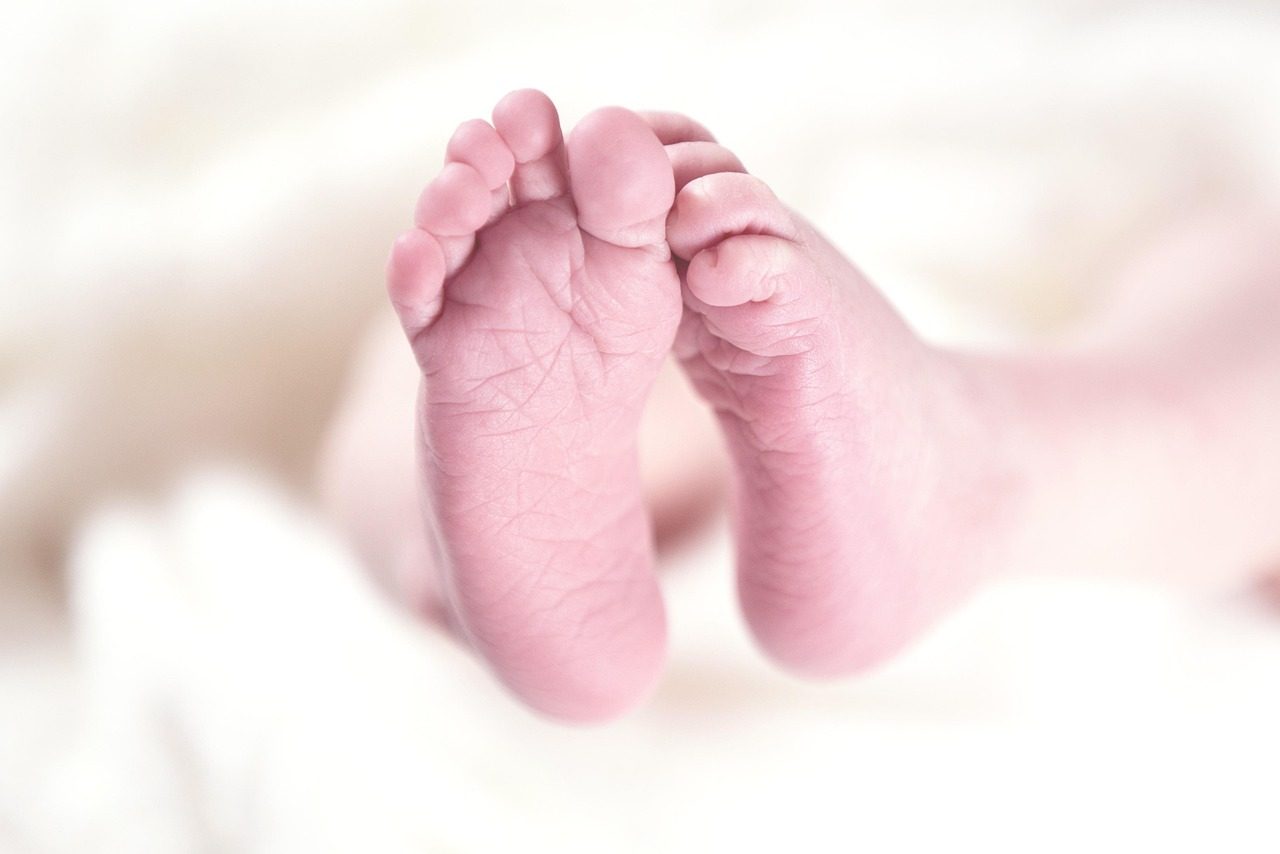 The bare feet of a newborn baby resting on a blanket