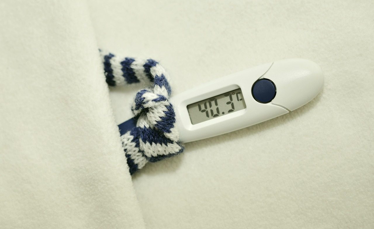 Digital thermometer reading 40.3 degrees Celsius beside a striped scarf on a blanket