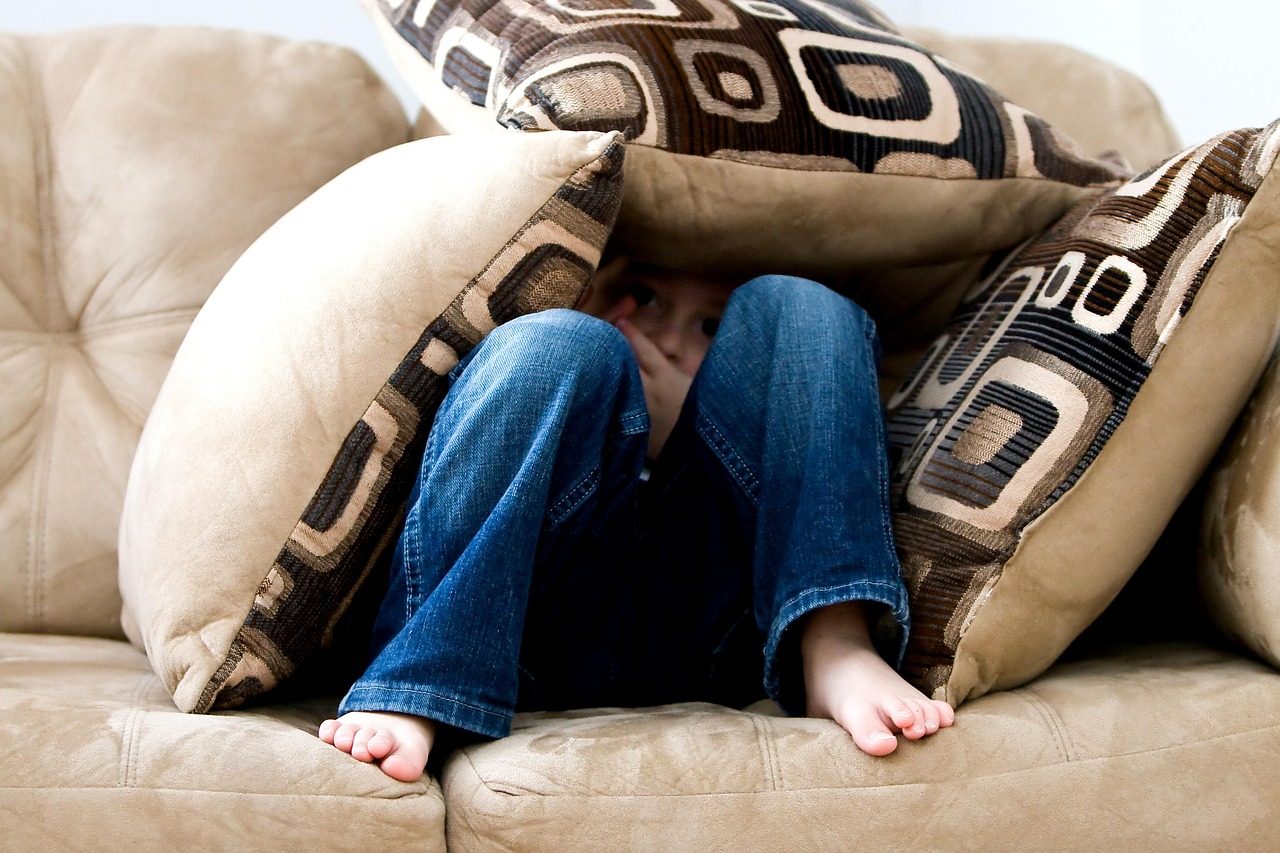 Illustrative stock photo of a young child hiding behind couch cushions, a model and not a victim