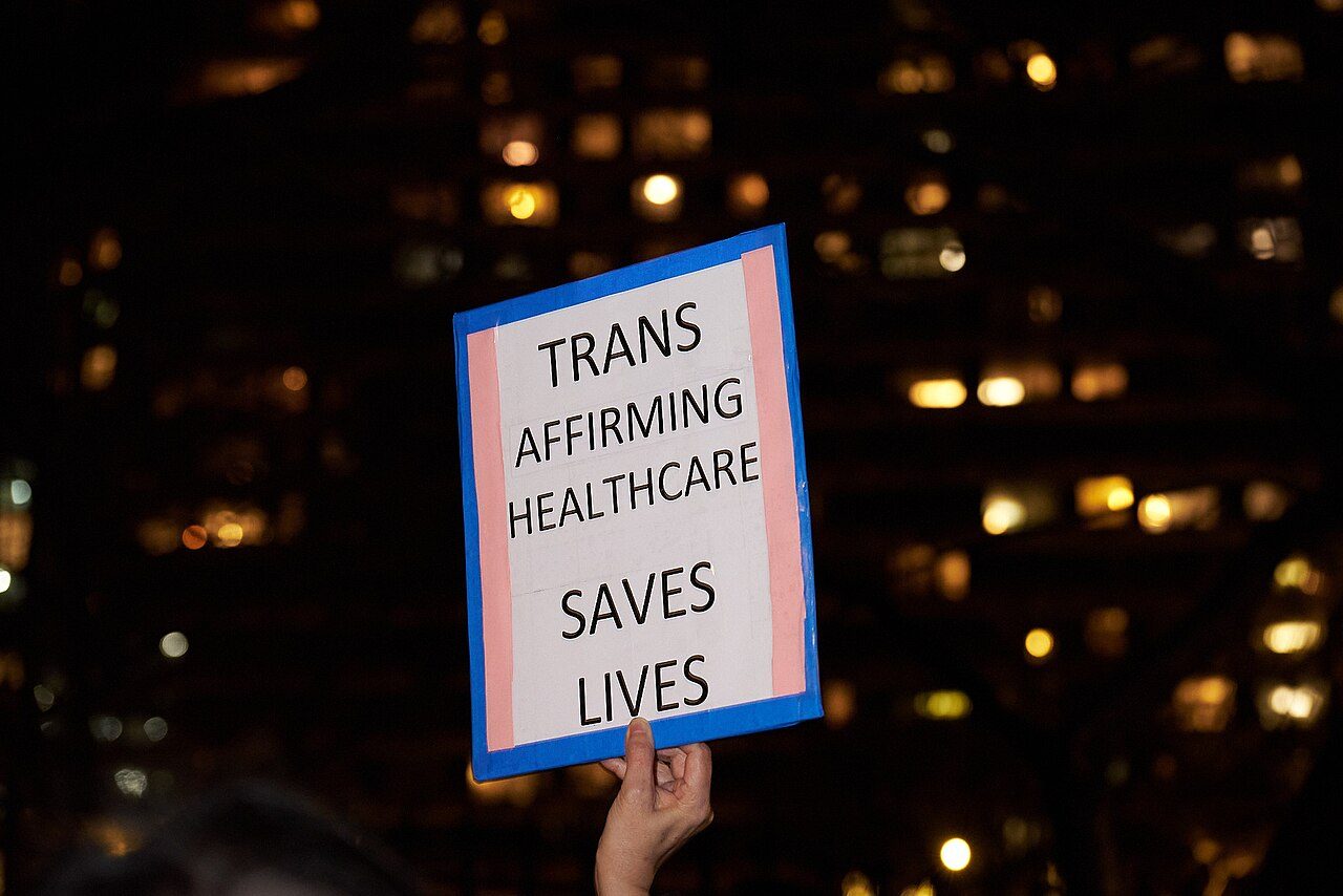 A protester holds up a sign supporting gender-affirming health care for transgender people