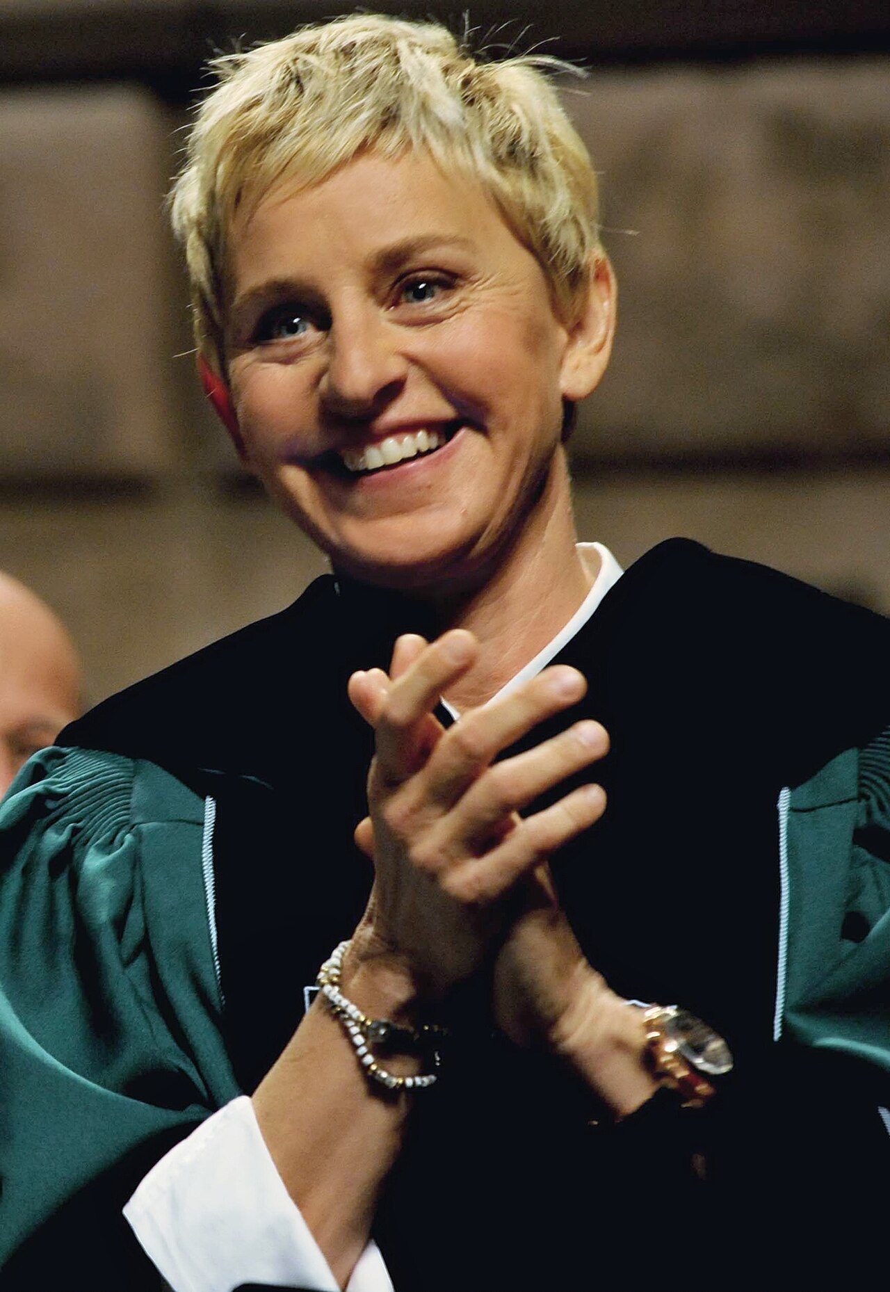 Ellen DeGeneres smiling and clapping in academic robes at Tulane University in 2009